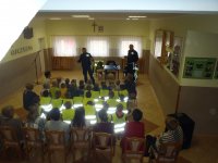 policjanci przeprowadzający prelekcję na tle dzieci w kamizelkach odblaskowych
