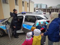Dzieci zwiedzają plac Komendy powiatowej Policji w Augustowie i oglądają radiowóz.