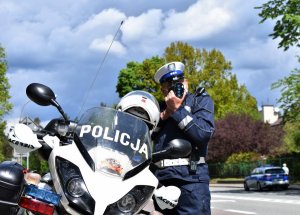 Policjant stoi przy motocyklu i mierzy prędkość.