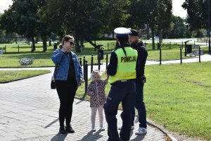 Policjantka wręcza dziecku oraz rodzicom elementy odblaskowe.