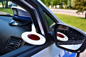 radiowóz z otwartym oknem przez, które widać czapkę funkcjonariusza ruchu drogowego i tarczę policyjną
policjant mierzy prędkość fotoradarem
policjantka siedzi i  pisze w radiowozie