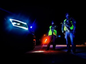 noc, stojący pojazd policyjny z włączonymi światłami. dwóch policjantów stoi przy radiowozie jeden trzyma w ręce latarkę święcącą na czerwono.
