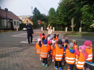 Policjant pokazuje dzieciom, jak należy prawidłowo przez przez przejście dla pieszych.