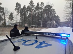 Policjanci stoją przy radiowozie. W tle aura zimowa.