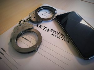 Telefon leży na aktach sprawy. Obok kajdanki.