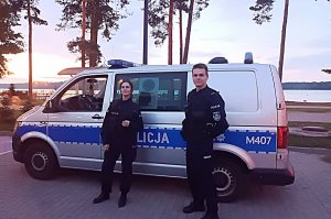 policjant i policjantka stoją przy radiowozie