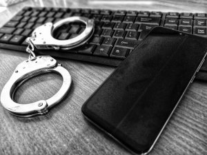 czarny blat na którym leży klawiatura od komputera na klawiaturze leżą kajdanki policyjne oraz prostokątny czarny portfel.
