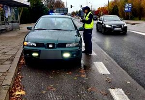 ulica, na ulicy stoi policjantka i kontroluje zielony pojazd marki seat, który jechał bez zapalonych świateł mijania