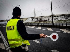 umundurowany policjant w kamizelce odblaskowej zatrzymuje pojazd do kontroli drogowej