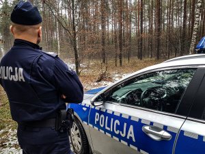 policyjny radiowóz stoi w lesie obok radiowozu stoi policjant