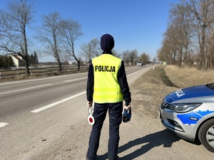 policjantka stoi odwrócona plecami i trzyma w jednej ręce fotoradar a w drugiej tarczę do zatrzymywania pojazdów