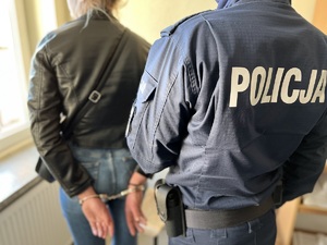 policjant trzyma kobietę za rękę, stoją odwróceni plecami