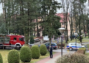 policjant idzie w stronę wejścia do szkoły w tle widać pojazd straży pożarnej i policji z włączonymi sygnałami świetlnymi