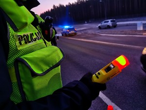 noc, policjant trzyma w ręce alkomat koloru żółtego, który świeci na czerwono