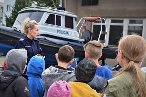 Policjantka stoi przy policyjnej łodzi służbowej i rozmawia z uczniami.
