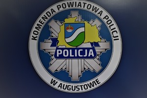 Logo komendy powiatowej policji w Augustowie na granatowym tle.