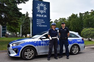 Policjant i policjantka stoją przy radiowozie.