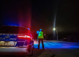 Zdjęcie nocą , policjant stoi tyłem.